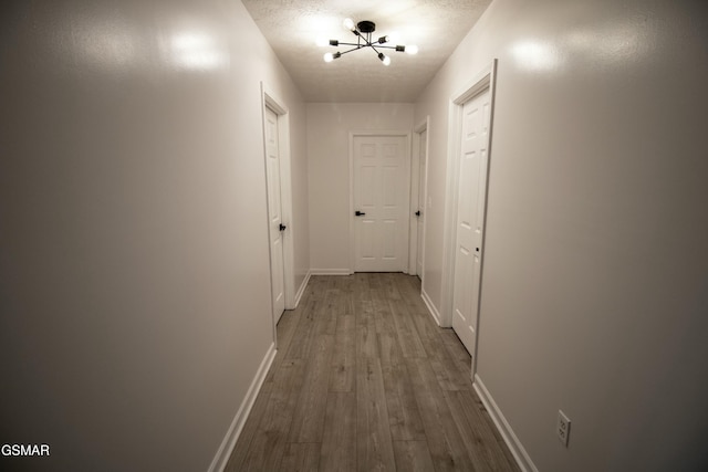 hallway featuring a chandelier, dark wood-style flooring, and baseboards