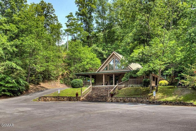 log-style house featuring driveway, a porch, stairway, and a view of trees