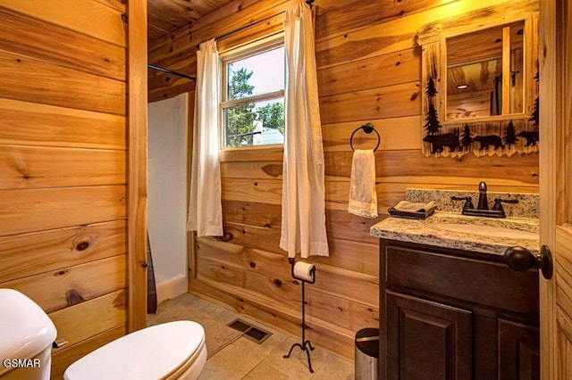 bathroom with a shower, visible vents, toilet, wooden walls, and vanity