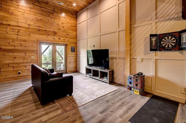 living area featuring wood ceiling, wood finished floors, a high ceiling, french doors, and a decorative wall