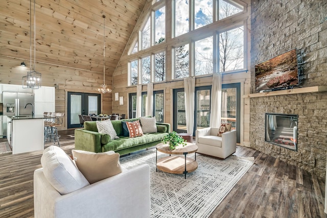 living room with french doors, dark hardwood / wood-style flooring, a high ceiling, a stone fireplace, and an inviting chandelier