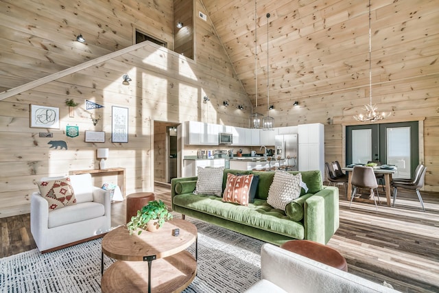 living room with french doors, sink, high vaulted ceiling, a notable chandelier, and wooden walls