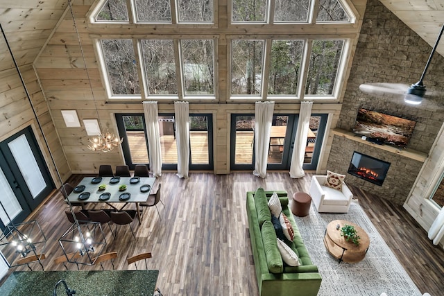 living room with hardwood / wood-style floors, wooden walls, high vaulted ceiling, and a stone fireplace