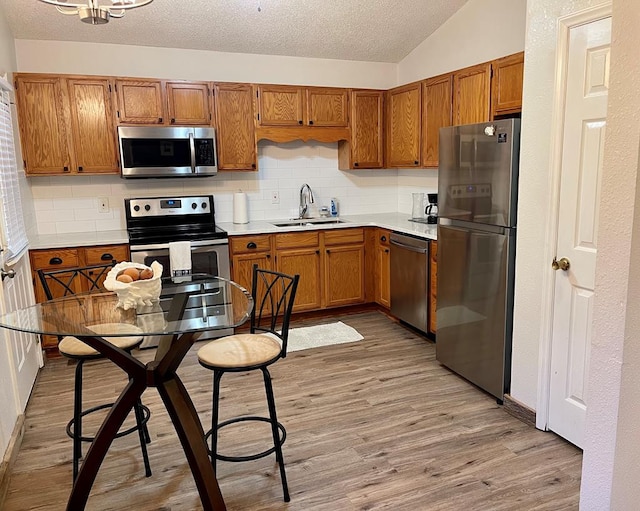 kitchen with stainless steel appliances, light countertops, brown cabinetry, a sink, and light wood-type flooring