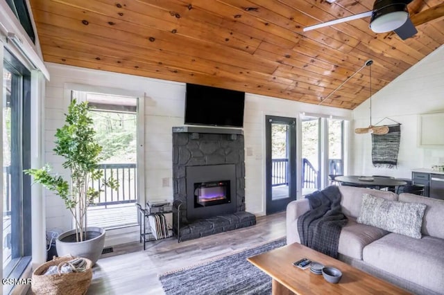 living room featuring ceiling fan, wooden ceiling, a stone fireplace, wood-type flooring, and lofted ceiling