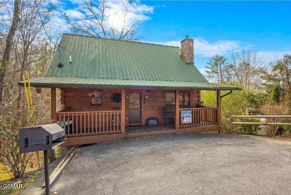 chalet / cabin with covered porch, a chimney, fence, and metal roof