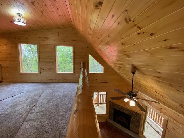 bonus room featuring lofted ceiling, a fireplace, ceiling fan, wooden walls, and wood ceiling