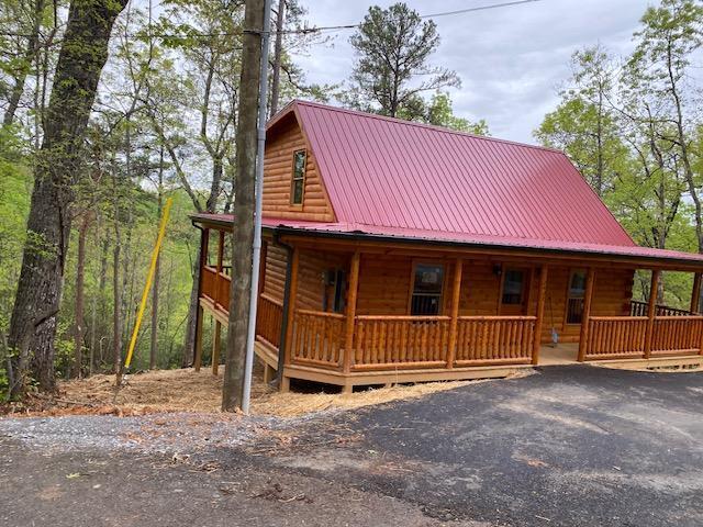 chalet / cabin featuring log veneer siding, covered porch, driveway, and metal roof