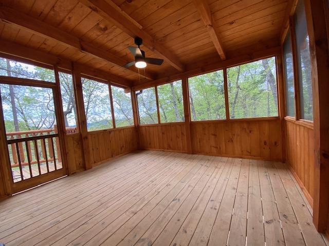 unfurnished sunroom featuring beamed ceiling, ceiling fan, and wood ceiling