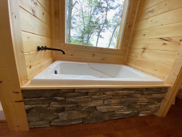 bathroom with tiled tub and wooden walls