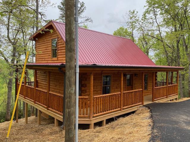 view of front of house with covered porch, metal roof, and log veneer siding