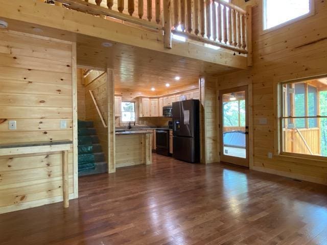 unfurnished living room featuring wood walls, a high ceiling, dark wood-style floors, and stairway