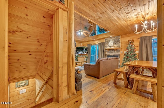 interior space with wood walls, wood-type flooring, a fireplace, wood ceiling, and ceiling fan with notable chandelier