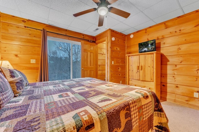 carpeted bedroom featuring ceiling fan, wood walls, and a drop ceiling