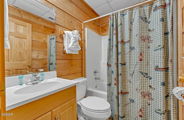 full bathroom featuring a drop ceiling, wood walls, vanity, toilet, and shower / tub combo with curtain