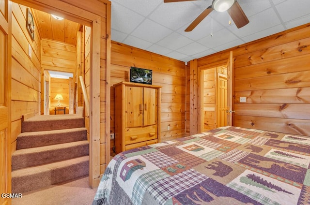 bedroom with ceiling fan, wooden walls, and a drop ceiling