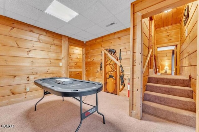 game room featuring a paneled ceiling, wood walls, and carpet floors