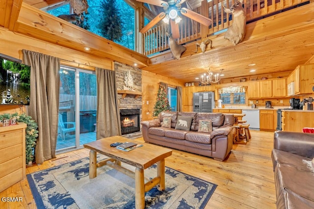 living room with ceiling fan with notable chandelier, a stone fireplace, light wood-type flooring, and a high ceiling