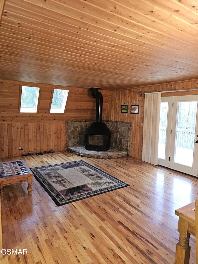 unfurnished living room with light hardwood / wood-style flooring, wooden walls, a healthy amount of sunlight, wooden ceiling, and a wood stove