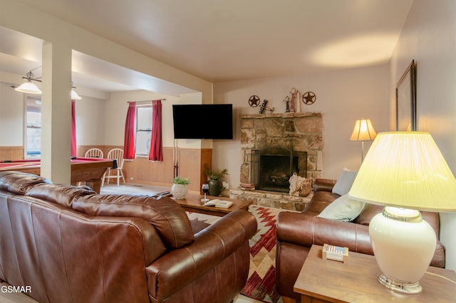 living area featuring a wainscoted wall, a stone fireplace, and a wealth of natural light