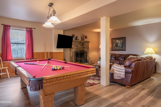 game room featuring a wainscoted wall, a stone fireplace, wood walls, and wood finished floors