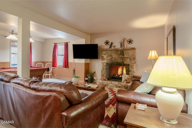 living room with a stone fireplace, wainscoting, and a healthy amount of sunlight