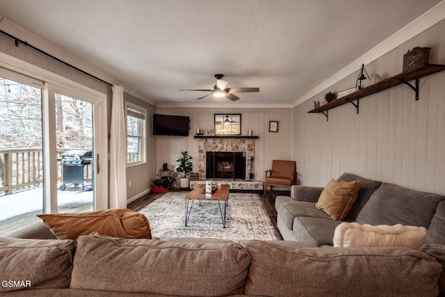 living room with a stone fireplace, wood finished floors, and a ceiling fan