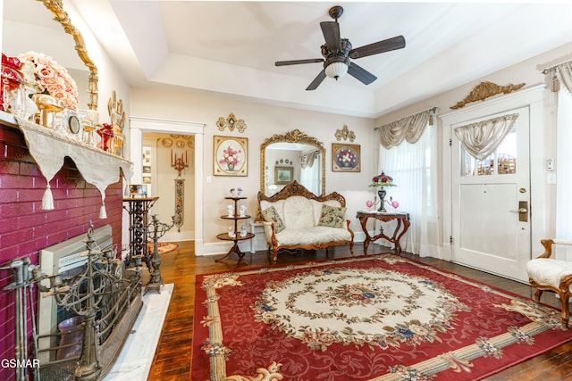 living area with a raised ceiling, ceiling fan, and dark wood-type flooring