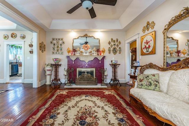 living room featuring a raised ceiling, ceiling fan, dark hardwood / wood-style flooring, and a fireplace