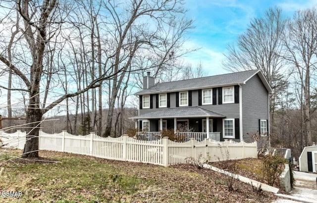 colonial home featuring a fenced front yard, a chimney, and a porch