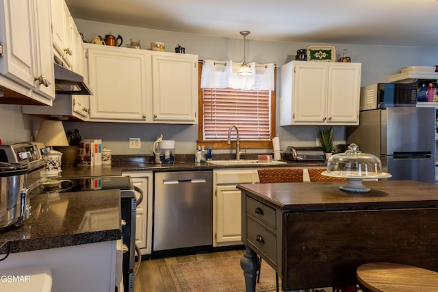 kitchen with stainless steel appliances, wood finished floors, a sink, white cabinetry, and dark countertops