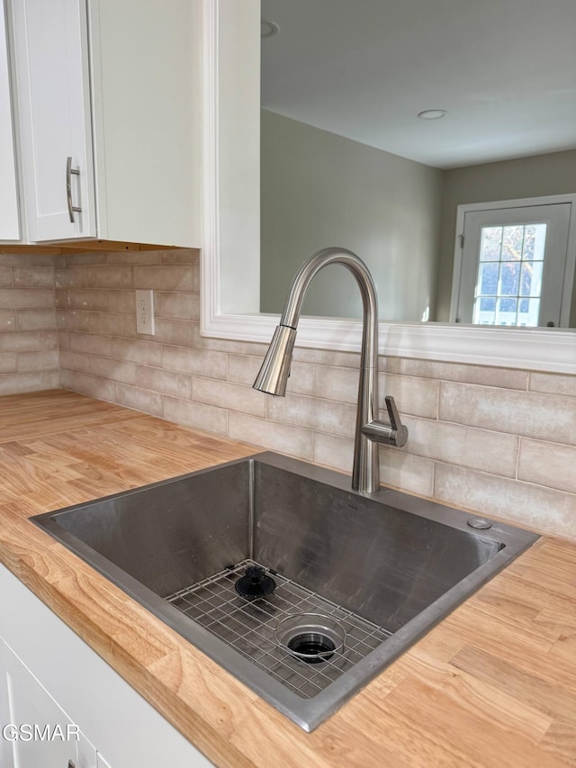 interior details featuring butcher block counters, sink, white cabinets, and backsplash