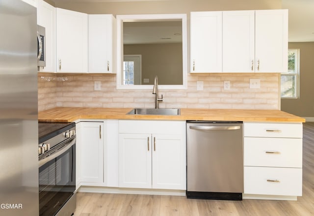 kitchen with white cabinetry, stainless steel appliances, butcher block counters, and sink