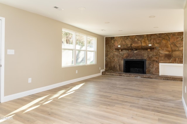 unfurnished living room featuring a stone fireplace and light hardwood / wood-style flooring