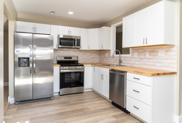 kitchen featuring butcher block countertops, sink, appliances with stainless steel finishes, white cabinets, and decorative backsplash