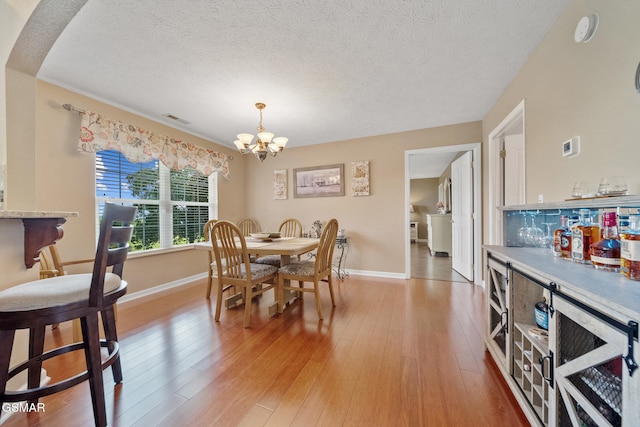 854 River Cliff Dr, Kodak, TN 37764 - dining space with a chandelier, a textured ceiling, baseboards, light wood finished floors, and a bar