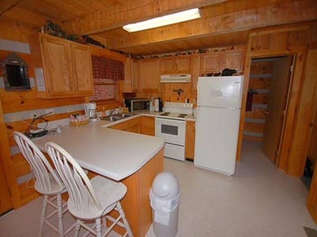 kitchen featuring kitchen peninsula, white appliances, a breakfast bar area, and sink