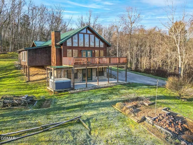 back of property with a wooden deck, stone siding, a hot tub, and a yard