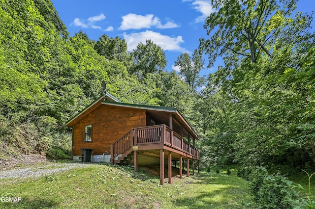 exterior space with a deck, stairway, a view of trees, and a lawn