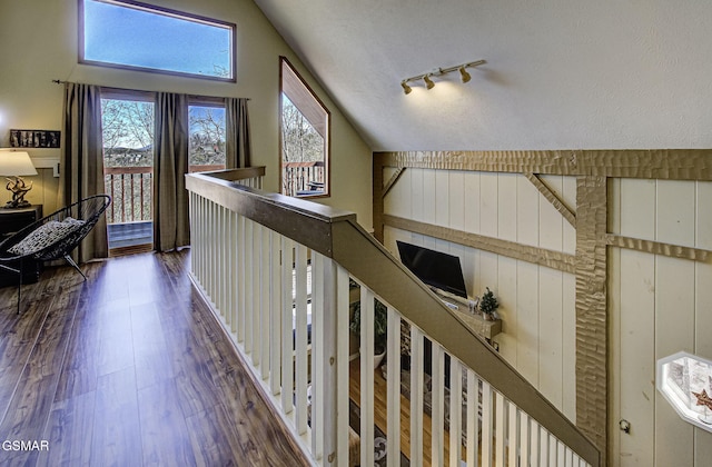 corridor with high vaulted ceiling, rail lighting, a textured ceiling, and wood finished floors