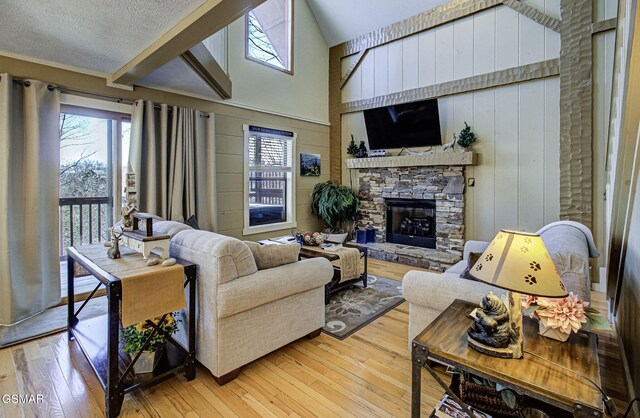 living room with a textured ceiling, high vaulted ceiling, light wood finished floors, and a fireplace