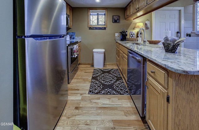 kitchen featuring brown cabinetry, a peninsula, light stone countertops, stainless steel appliances, and a sink