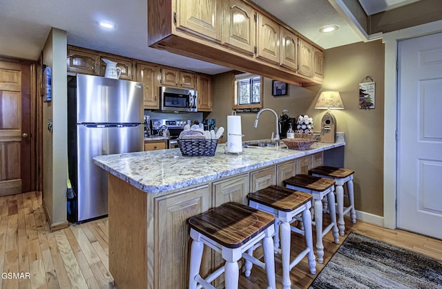 kitchen with stainless steel appliances, light wood-type flooring, a sink, and a peninsula