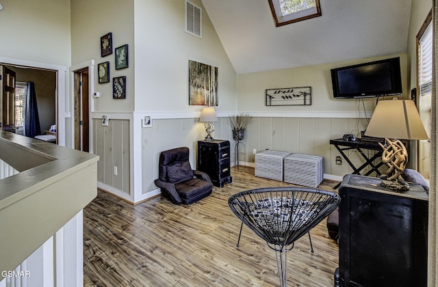 living room featuring a wainscoted wall, visible vents, vaulted ceiling, and wood finished floors