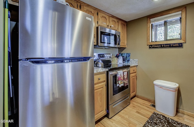 kitchen with baseboards, light wood-style flooring, appliances with stainless steel finishes, and a textured ceiling