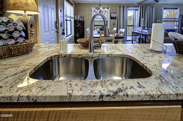 kitchen featuring a notable chandelier, a sink, hanging light fixtures, and light stone countertops