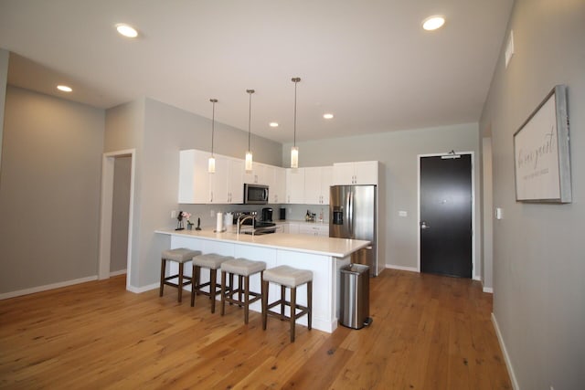 kitchen with stainless steel appliances, kitchen peninsula, decorative light fixtures, a breakfast bar, and white cabinets