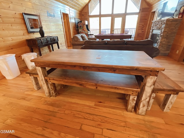 dining room featuring light wood-style flooring, vaulted ceiling, wood walls, and pool table