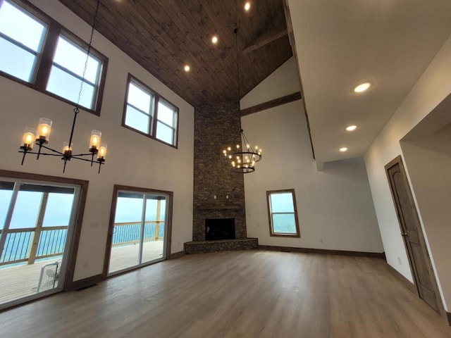 unfurnished living room with a stone fireplace, wood-type flooring, high vaulted ceiling, and an inviting chandelier