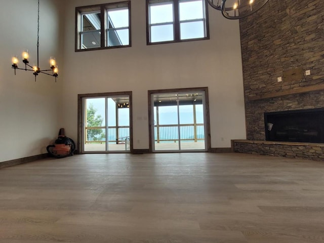 unfurnished living room featuring a stone fireplace, a wealth of natural light, hardwood / wood-style floors, and an inviting chandelier